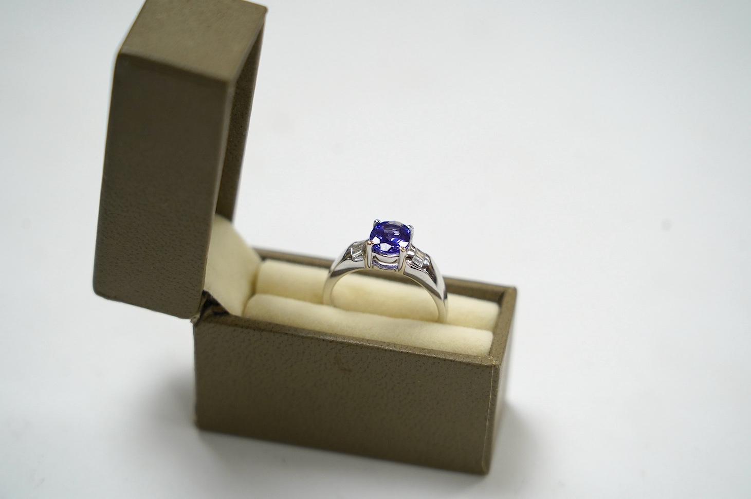 A modern 18ct gold and single stone oval cut tanzanite set ring, with baguette cut diamond cluster set shoulders, with accompanying AnchorCert report, stating the stone to weigh 1.20ct, size L, gross weight 4.1 grams. Co